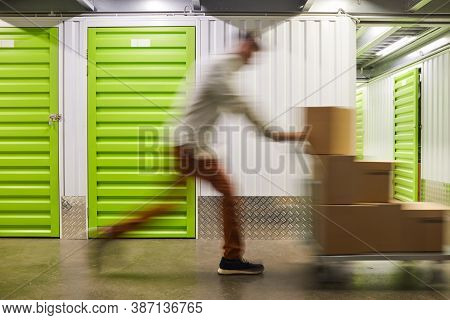 Blurred Motion Shot Of Unrecognizable Man Pushing Cart With Boxes While Running In Self Storage Faci