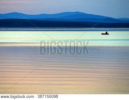 Calm Blue Sunset Sky Over The Lake, Silhouette Of A Lone Boat With A Fisherman, Calm Surface Of Wate