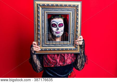 Young woman wearing day of the dead costume holding empty frame looking positive and happy standing and smiling with a confident smile showing teeth 