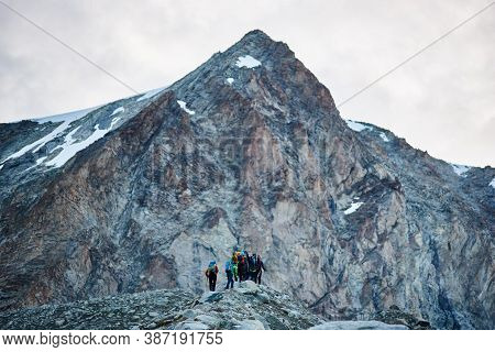 Zinal, Switzerland - July 19, 2019: Back View Of Hikers Team With Backpacks Walking On Rocky Path An
