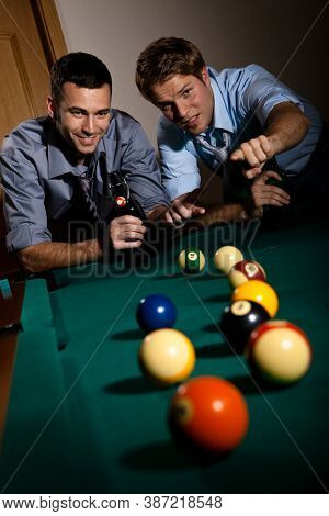 Happy friends discussing a game of billiard at table with beer in hand. Selective focus, pointing. Having fun.