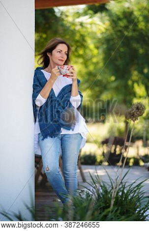 Mature Woman With Cup Of Tea Resting Outdoors In Backyard.