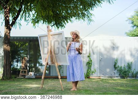 Portrait Of Mature Woman With Pallete Painting Outdoors In Garden.