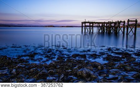 Fine Art Image Showing Old Broken Wooden Pier Remains In Calm Water (blurred) With Inchcolm Island A