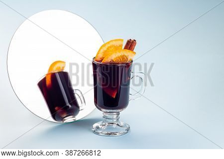 Glass Of Red Glogg Or Mulled Wine With Orange Slices And Cinnamon Stick Near Mirror, On A Blue Backg