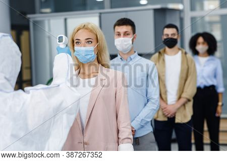 Temperature Control Test At Work And Social Distancing. Man In Protective Suit Checks Multinational 