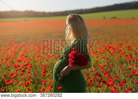 Beautiful Blonde Pregnant Woman In Long Green Dress With A Bunch Of Flowers In Hand, In The Middle O