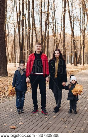 Caucasian Family Goes For A Walk In The Autumn Park With Two Children