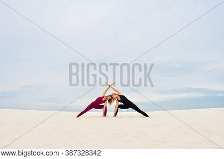 Two Beautiful Young Women Performing Yoga Pose Parshvakonasana Together On The Beach