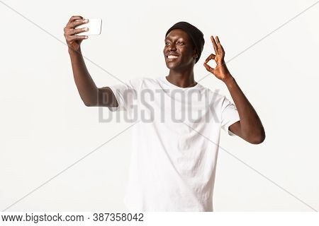Satisfied, Smiling African-american Young Guy In Beanie, Taking Selfie Or Video Call Via Smartphone,