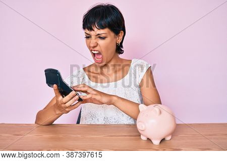 Beautiful brunettte woman caculating money savings angry and mad screaming frustrated and furious, shouting with anger. rage and aggressive concept. 