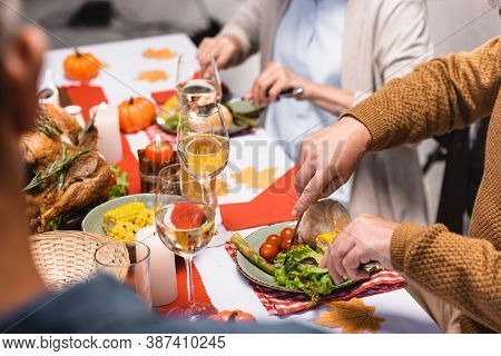 Focus Of Senior Man Cutting Lettuce Near Family During Thanksgiving Dinner