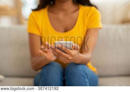 Closeup View Of Young Black Woman Using Mobile Phone For Work Or Studies On Sofa At Home. African Am