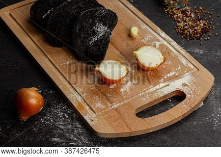 Fresh Black Rye Bread On A Cutting Board With Seasonings Sprinkled With Flour On A Black Wooden Tabl