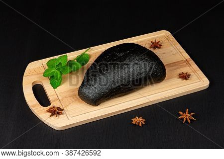Fresh Black Rye Bread On A Cutting Board With Seasonings Sprinkled On A Black Wooden Table