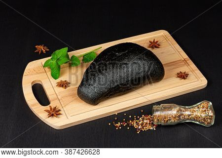 fresh black rye bread on a cutting board with seasonings sprinkled with flour on a black wooden tabl