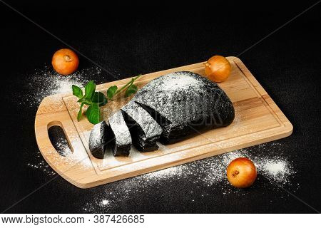 fresh black rye bread on a cutting board with seasonings sprinkled with flour on a black wooden tabl