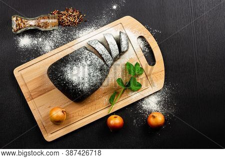 Fresh Black Rye Bread On A Cutting Board With Seasonings Sprinkled With Flour On A Black Wooden Tabl