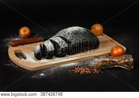 Fresh Black Rye Bread On A Cutting Board With Seasonings Sprinkled With Flour On A Black Wooden Tabl