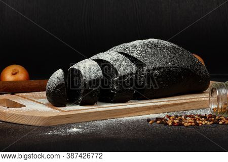 Fresh Black Rye Bread On A Cutting Board With Seasonings Sprinkled With Flour On A Black Wooden Tabl