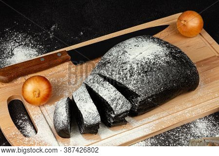 Fresh Black Rye Bread On A Cutting Board With Seasonings Sprinkled With Flour On A Black Wooden Tabl