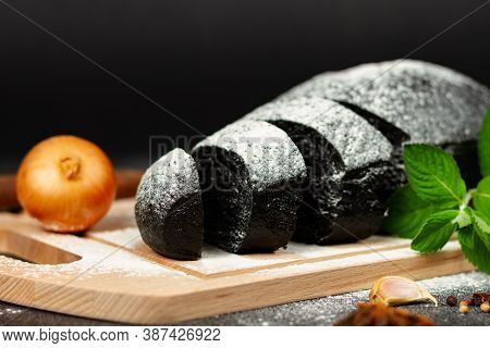 Fresh Black Rye Bread On A Cutting Board With Seasonings Sprinkled With Flour On A Black Wooden Tabl