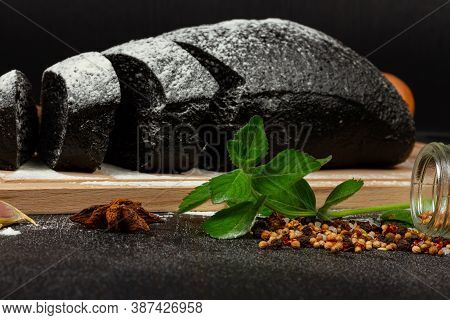 Fresh Black Rye Bread On A Cutting Board With Seasonings Sprinkled With Flour On A Black Wooden Tabl
