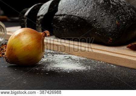 Fresh Black Rye Bread On A Cutting Board With Seasonings Sprinkled With Flour On A Black Wooden Tabl