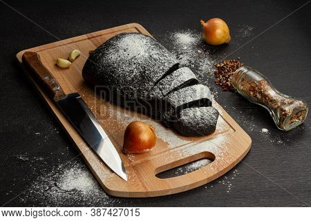 Fresh Black Rye Bread On A Cutting Board With Seasonings Sprinkled With Flour On A Black Wooden Tabl