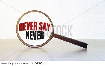 Magnifying Glass With Text Never Say Never On Wooden Table.