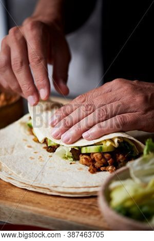 closeup of a young caucasian man preparing a durum or a burrito, with chicken meat, lettuce and cucumber