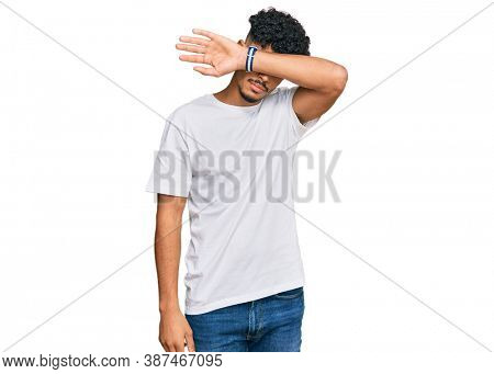 Young arab man wearing casual white t shirt covering eyes with arm, looking serious and sad. sightless, hiding and rejection concept 