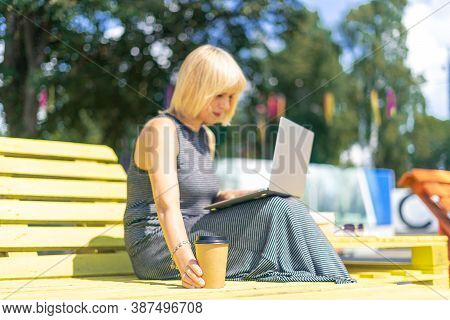 Adult Woman Having Video Call With Laptop Outside In Park. Happy And Smiling Senior Working And Drin