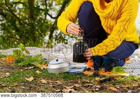 Young Beautiful Girl In A Yellow Sweater Makes Coffee In The Forest On A Gas Burner. Making Coffee O