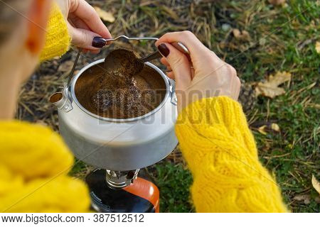 Young Beautiful Girl In A Yellow Sweater Makes Coffee In The Forest On A Gas Burner. Making Coffee O