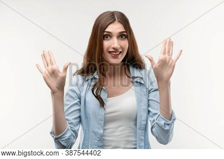 Studio Shot Of Surprised Young Female With Long Chestnut Hair, Dressed In Casual Clothes, Smiling Ha