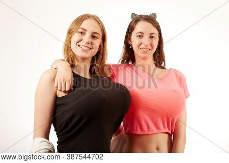 Young Women Showing Their Big Fake Breasts On White Background, Looking At Camera, Smiling