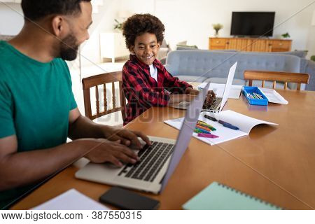 Mixed race man with son enjoying family time together at home, social distancing and self isolation in quarantine lockdown, using laptops and smiling
