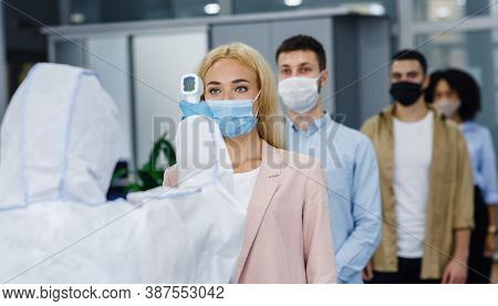 Health Control At Work And New Normal For Company. Man In Protective Suit Checks Temperature With In