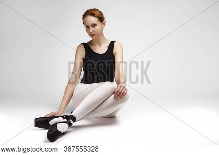 Relaxing Caucasian Professional Ballet Dancer In Body Suit  And Pointes Shoes Posing Against White B