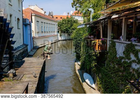 Old Water Mill Wheel And Sculpture Of Vodyanoy (water Demon) Near The Island Of Kampa With The River