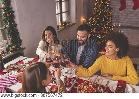High Angle View Of Group Of Friends Making A Toast During Christmas Dinner, Raising Glasses Of Wine 