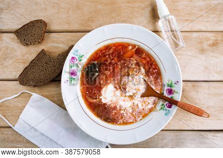 Russian Borshch And Medical Mask On Wooden Table. Coronavirus Concept. Social Distance Concept
