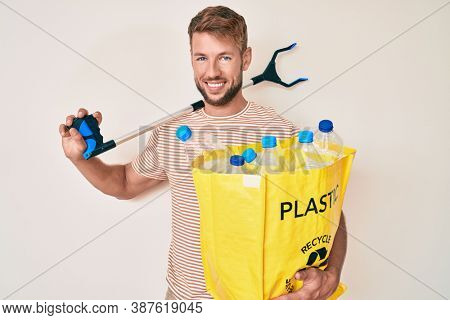 Young caucasian man holding recycling bag with plastic bottles and waste picker smiling with a happy and cool smile on face. showing teeth. 