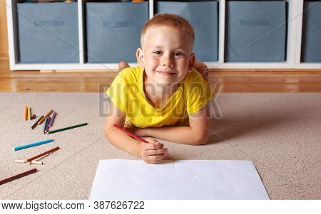 Cute Blond Boy Draws On Paper Lying On The Floor And Smiles. The Concept Of Educational Games, Extra