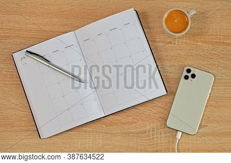 White Phone Charging, Opened Diary With Pen And Epresso Shot On Wooden Table From Above