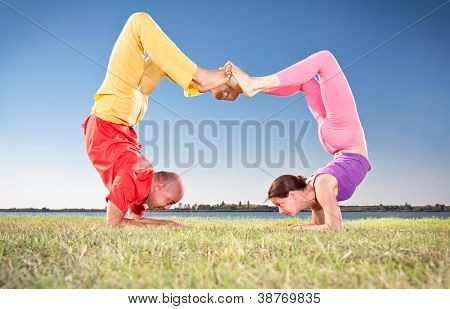 Yoga coppia, uomo e donna facendo Vrschikasana scorpion pongono sul banco di lago. Concetto di yoga.