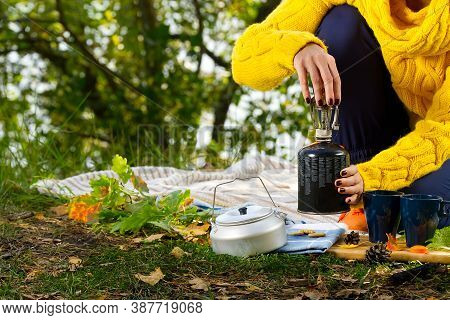 Young Beautiful Girl In A Yellow Sweater Makes Coffee In The Forest On A Gas Burner. Making Coffee O