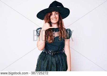 Young beautiful woman wearing witch halloween costume smiling doing phone gesture with hand and fingers like talking on the telephone. communicating concepts. 