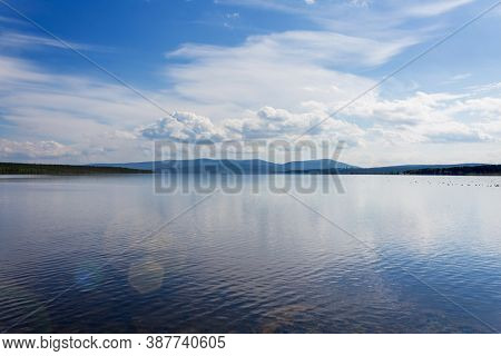 Pacifying Lake Landscape On Summer Sunny Day With Sunlight Flare. Blue Mountains Silhouette And Whit